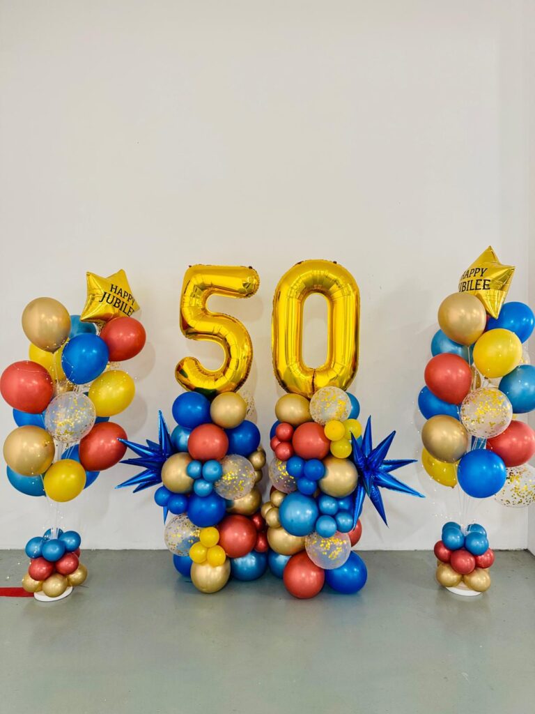 Gold foil 50 balloons and blue, red and gold balloon columns set up for Ritchmen&rsquo;s 50th anniversary.